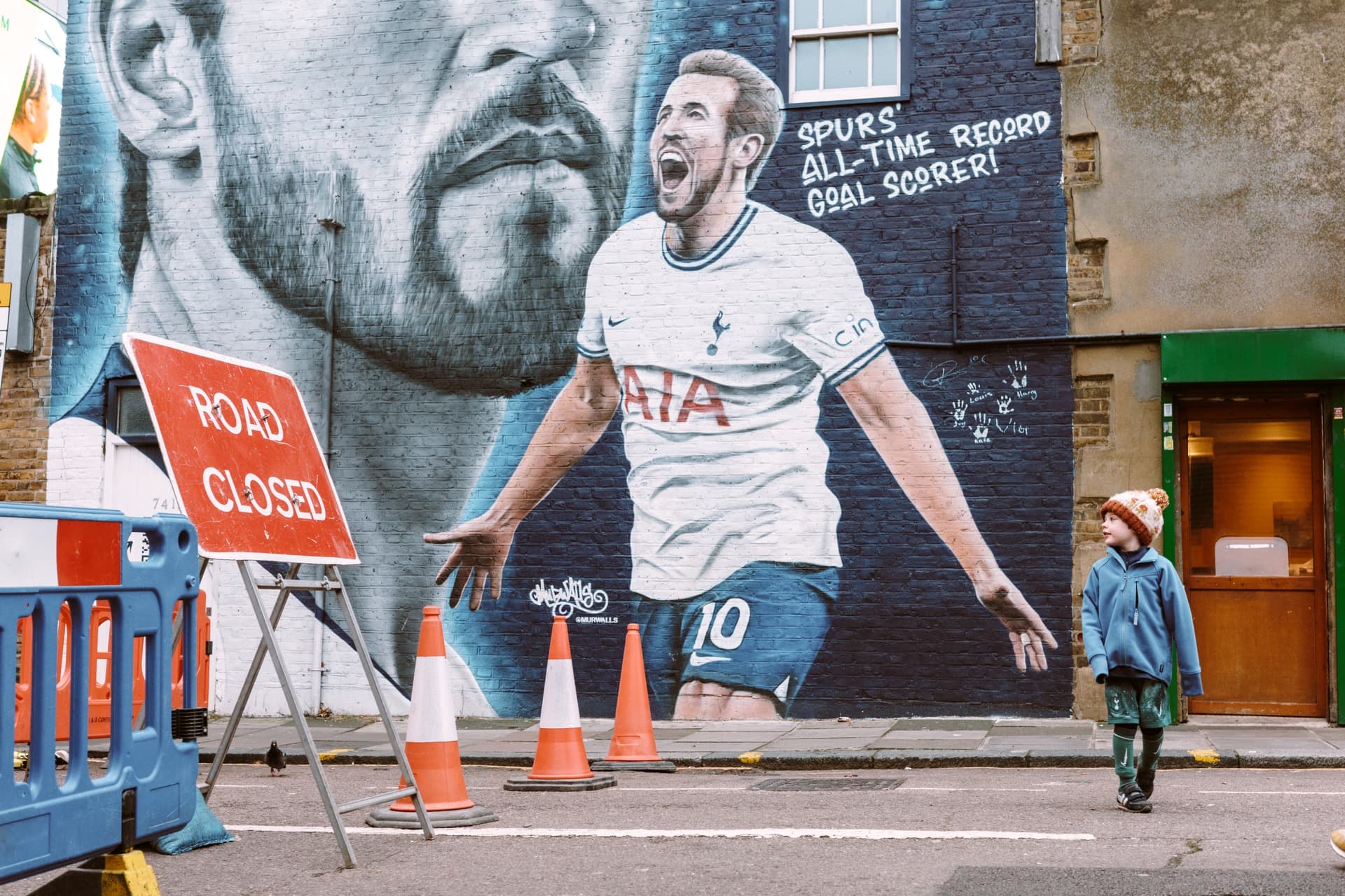 Kid standing in front of a Harry Kane mural